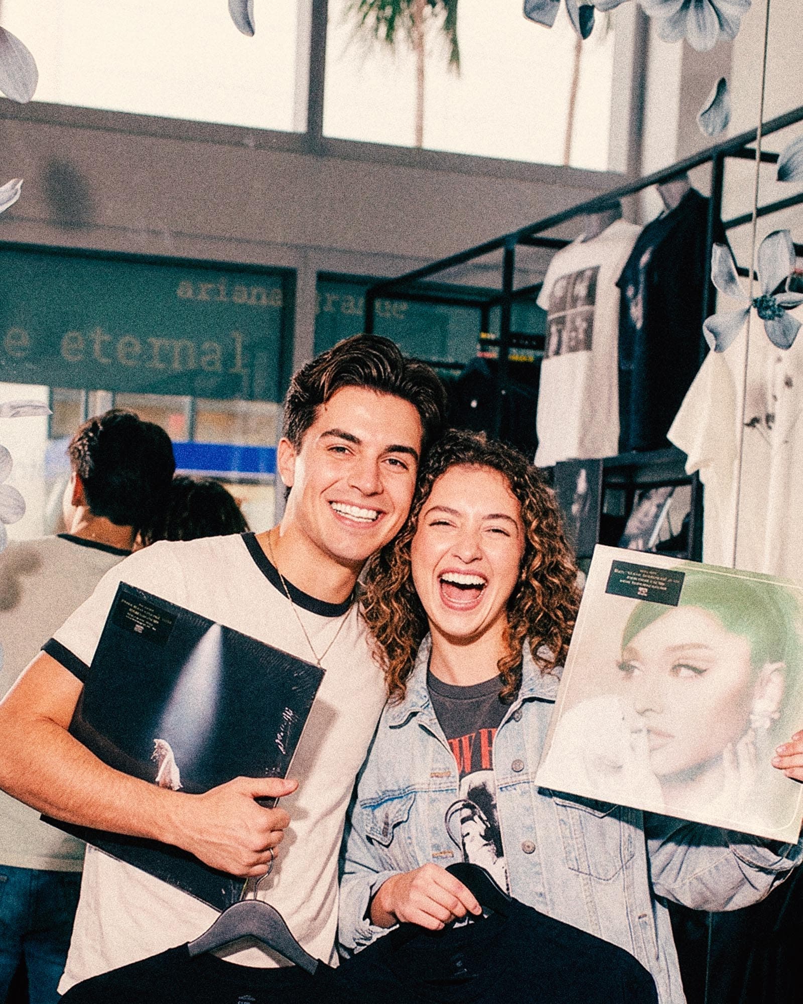 Two fans holding up their vinyl and merchandise at a pop-up store